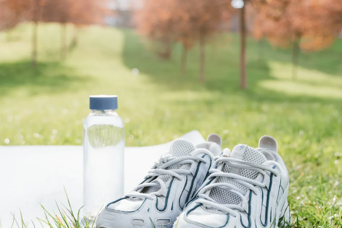 Running shoes and a clear water bottle resting on grass in a sunny park