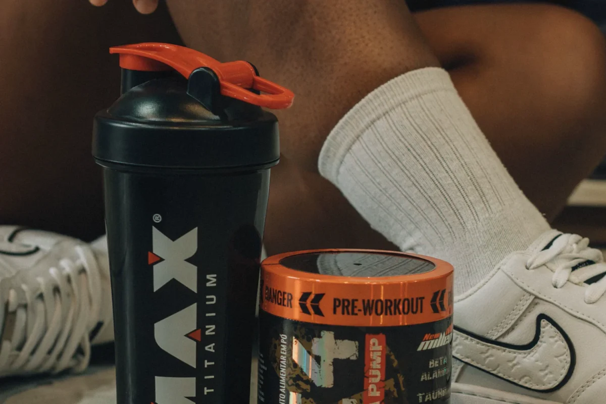 Tub of workout supplement beside a shaker bottle on a gym floor