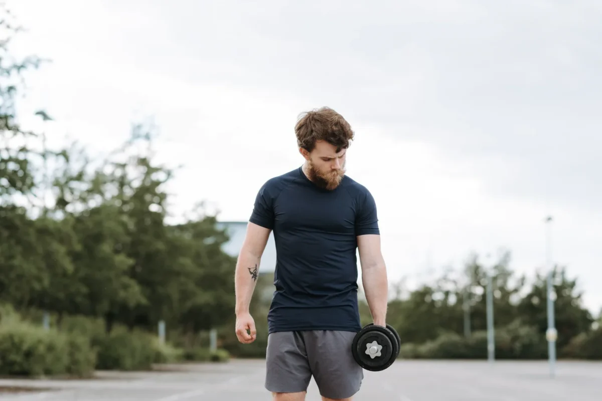 Man rebuilding his exercise routine with a controlled dumbbell curl at an outdoor training area